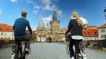 Two people riding bicycles on a cobblestone bridge with a historic building in the background.