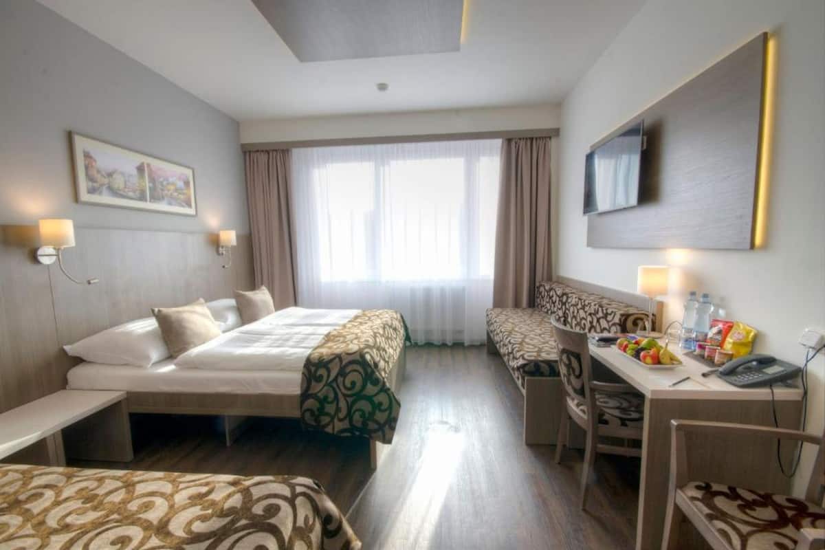 Habitación de hotel con dos camas, un escritorio con silla, televisión y ventana con cortinas.