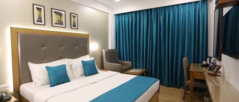 A hotel room with a large bed, a desk, a chair, a telephone, and a ceiling fan.