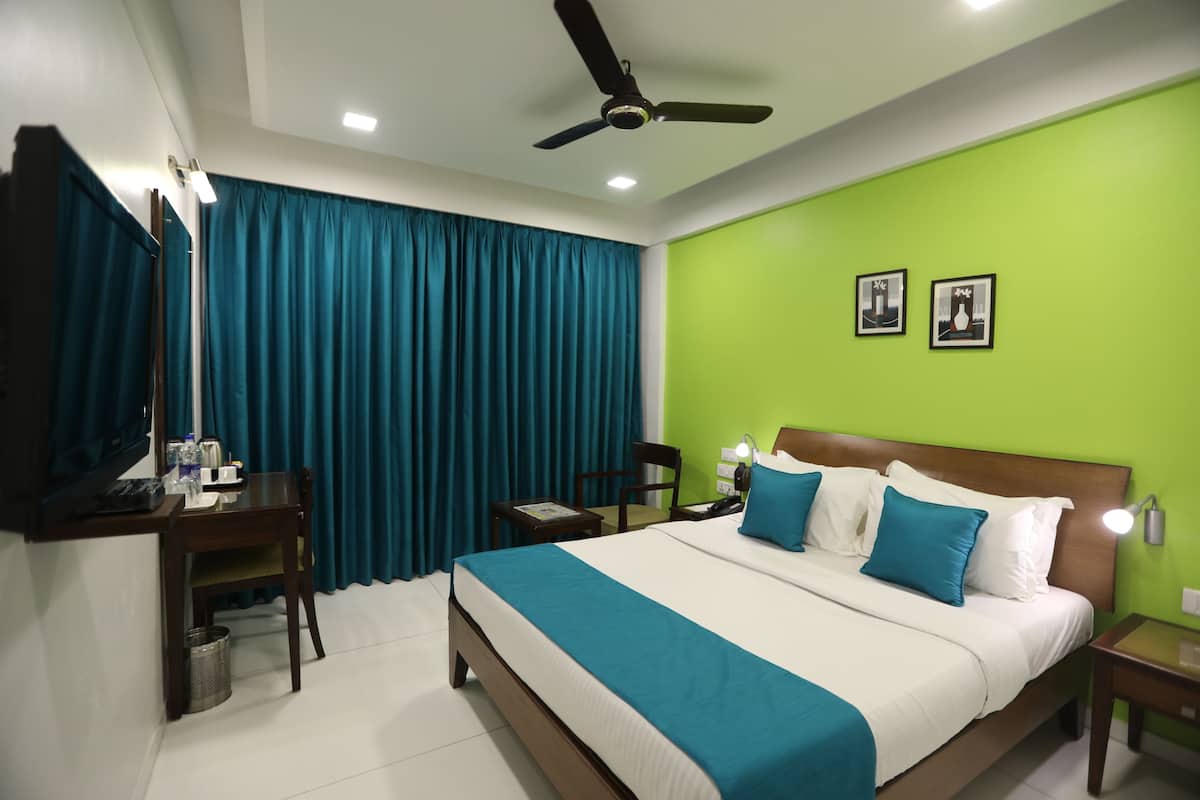 A hotel room with a bed, a desk, a chair, a ceiling fan, and a green wall.