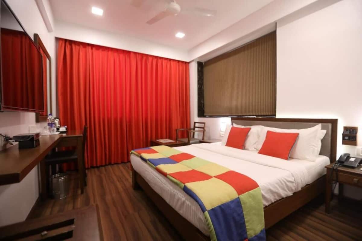 A hotel room with a bed, a desk, a chair, a telephone, and a window with curtains.