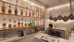 A bar area with shelves of liquor bottles, a bar counter, and a person serving. - Citizen Hotel (Mumbai)