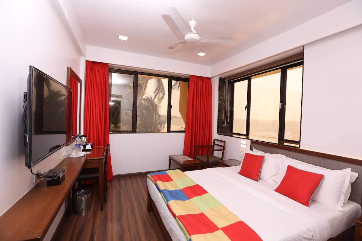 A hotel room with a bed, a desk, a television, and a window with red curtains.