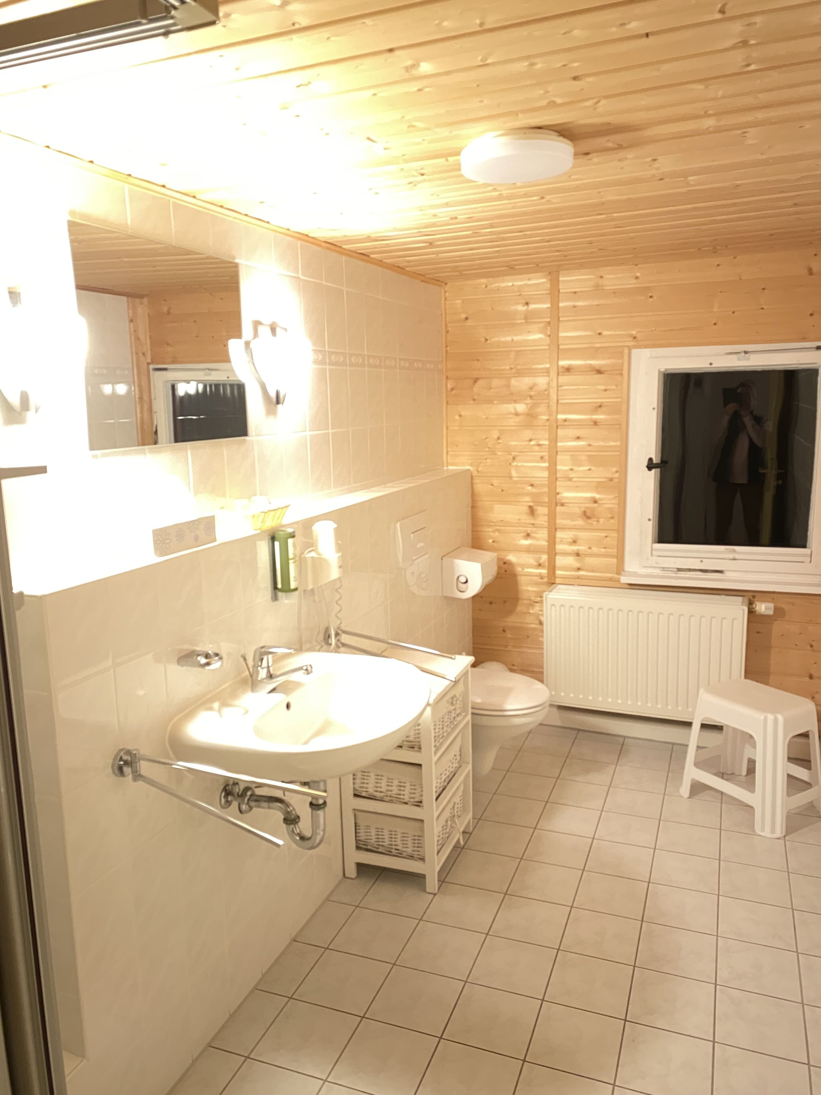 Ein Badezimmer mit einem weißen Waschbecken, einer Toilette, einem Fenster und einer Heizung.