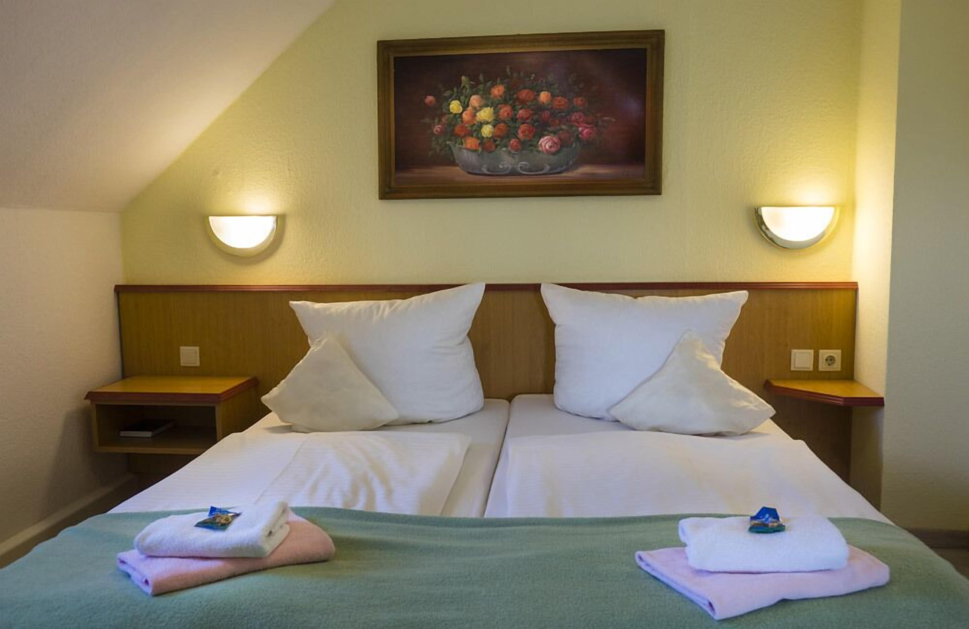A double bed with white linens, two bedside tables, and a painting of flowers on the wall.
