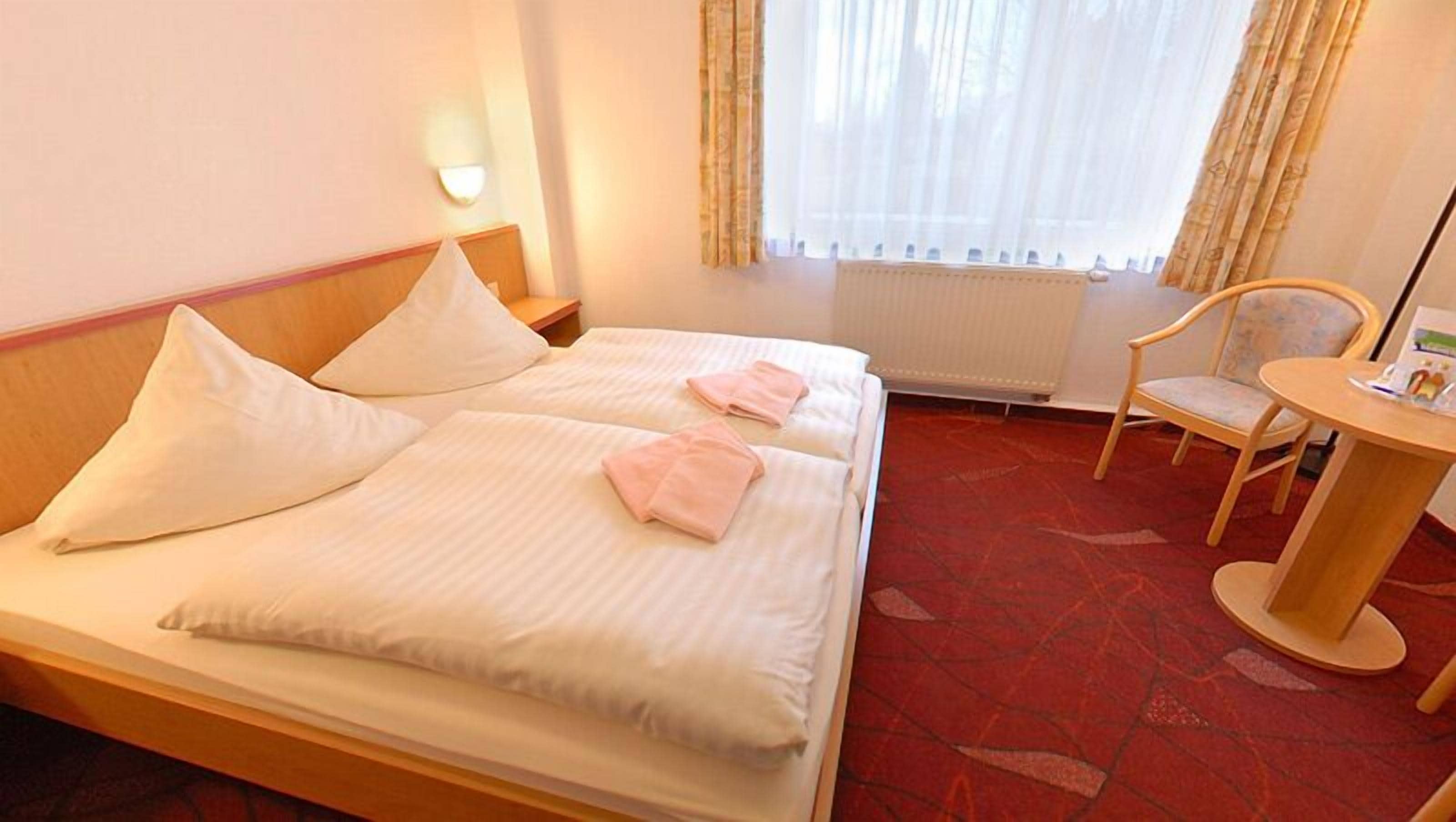 Una habitación de hotel con cama, almohadas, una silla y una mesita.