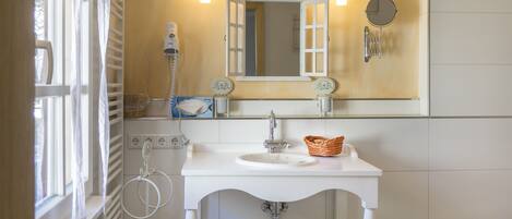 A bathroom with a white sink, a mirror with a white frame, a towel rack, and a window with white curtains.