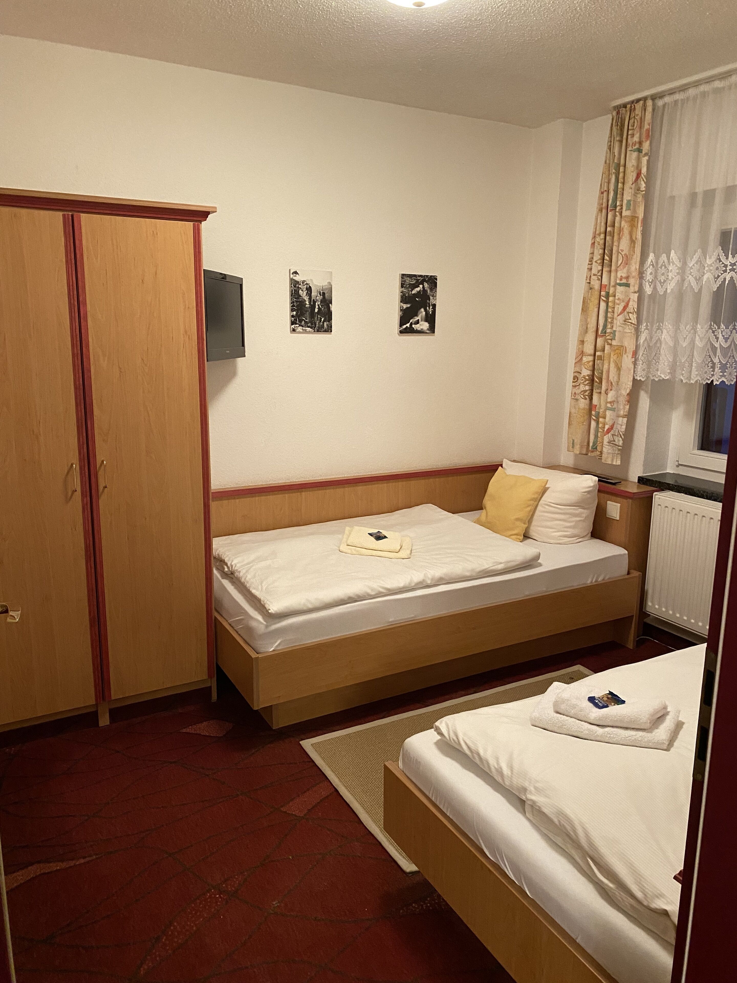 A hotel room with a single bed, a wardrobe, and two framed pictures on the wall.