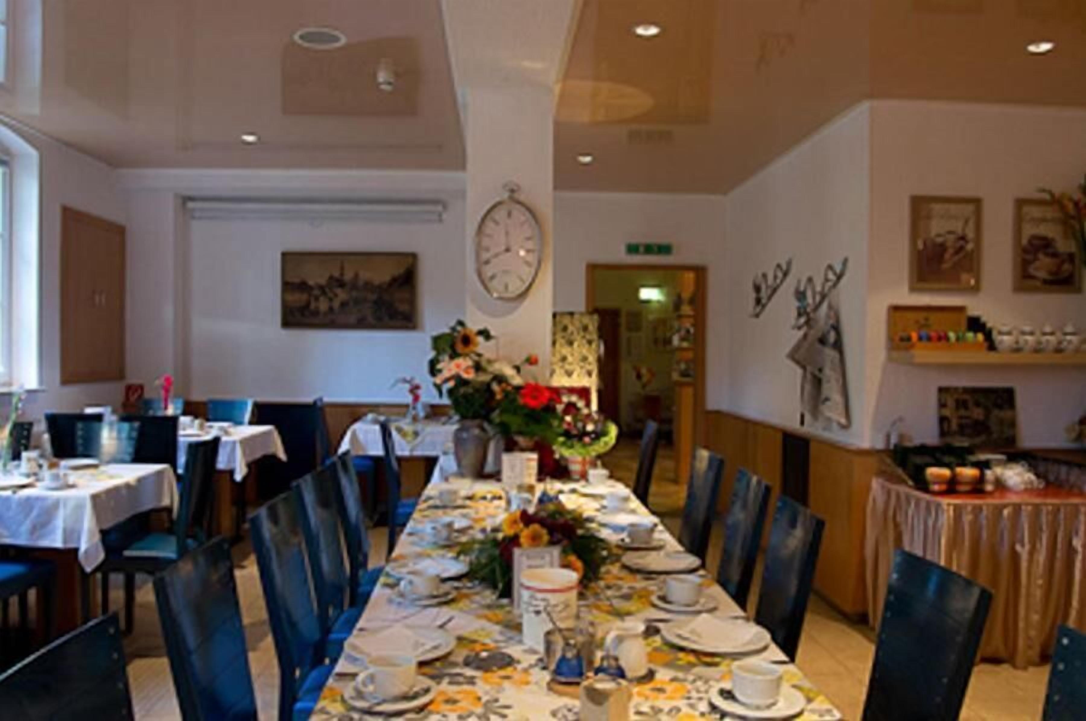 A dining area with a long table set for a meal, chairs around it, and a clock on the wall.