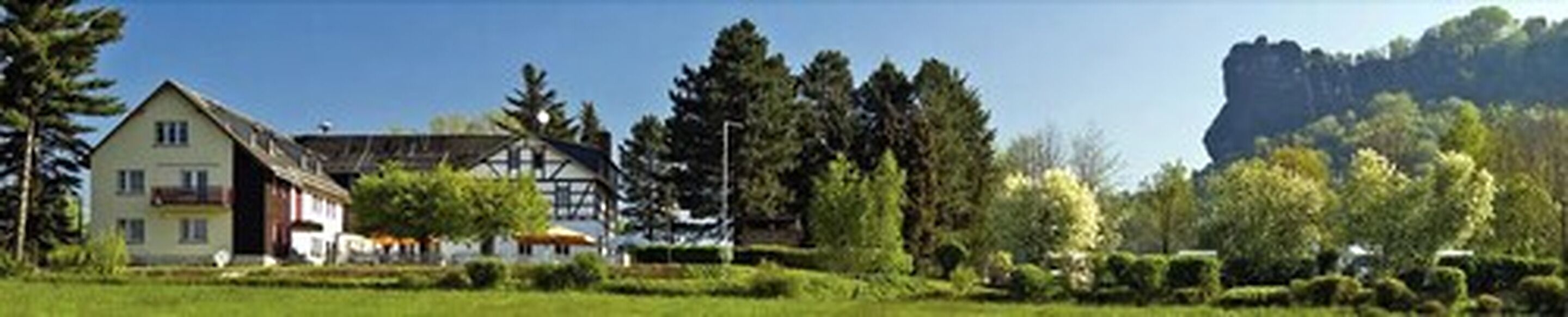 A traditional building with a sloped roof, surrounded by lush greenery and a prominent rock formation in the background.