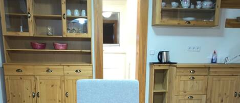 A compact kitchen with wooden cabinets, a dining chair, and a small table.