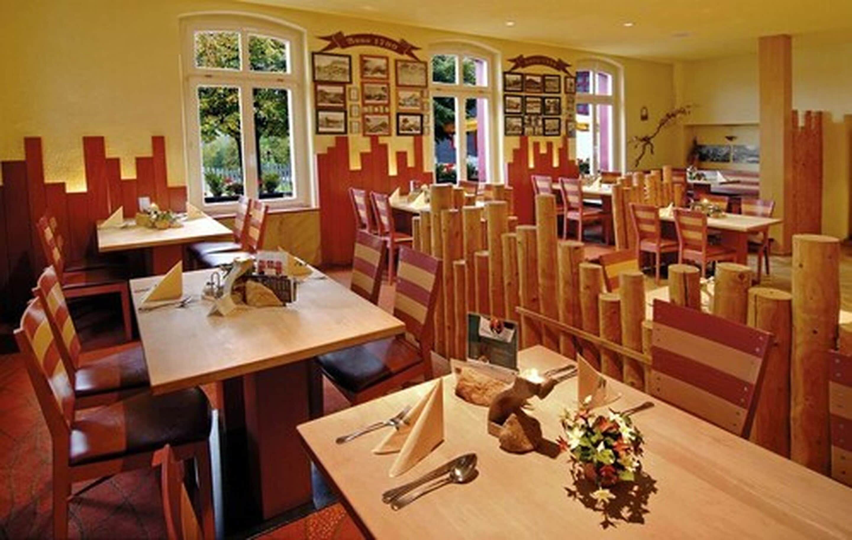 Een restaurant met houten zithoeken en tafels, ingelijste foto's aan de muur en grote ramen.