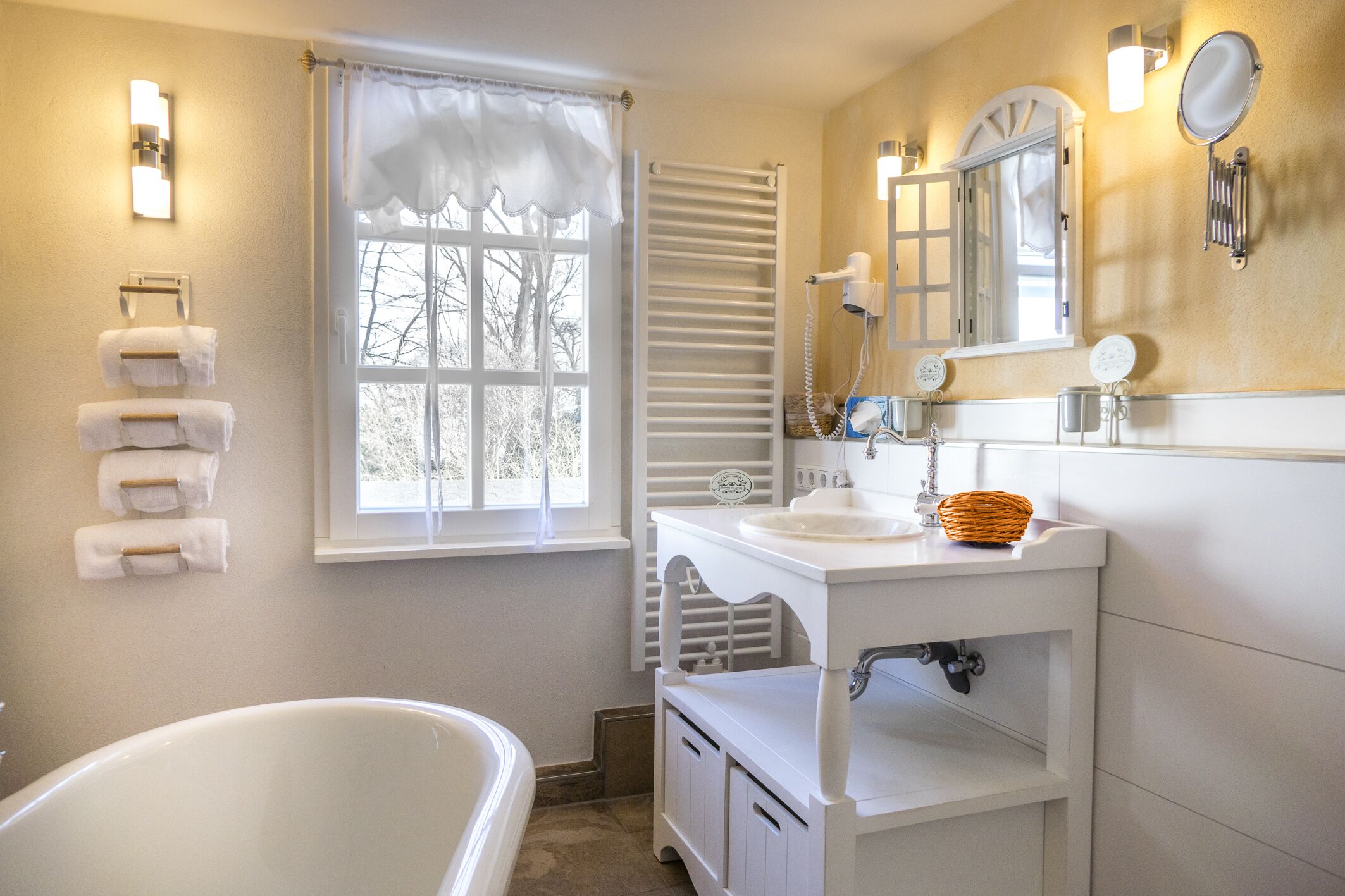 A bathroom with a bathtub, a window with white shutters, a towel rack, and a vanity with a mirror and sink.