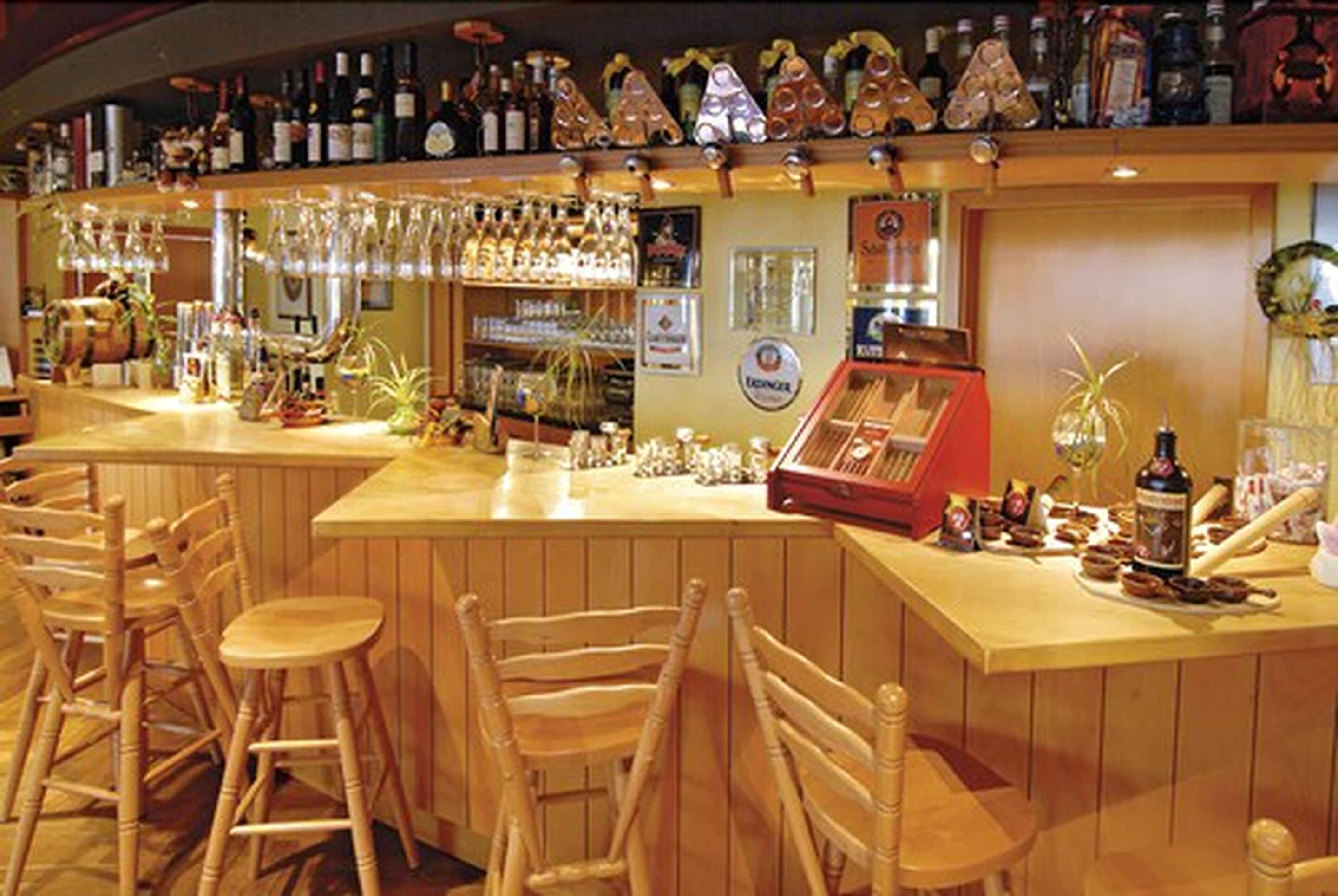 A bar area with wooden chairs, a counter with various bottles and glasses, and a cash register.