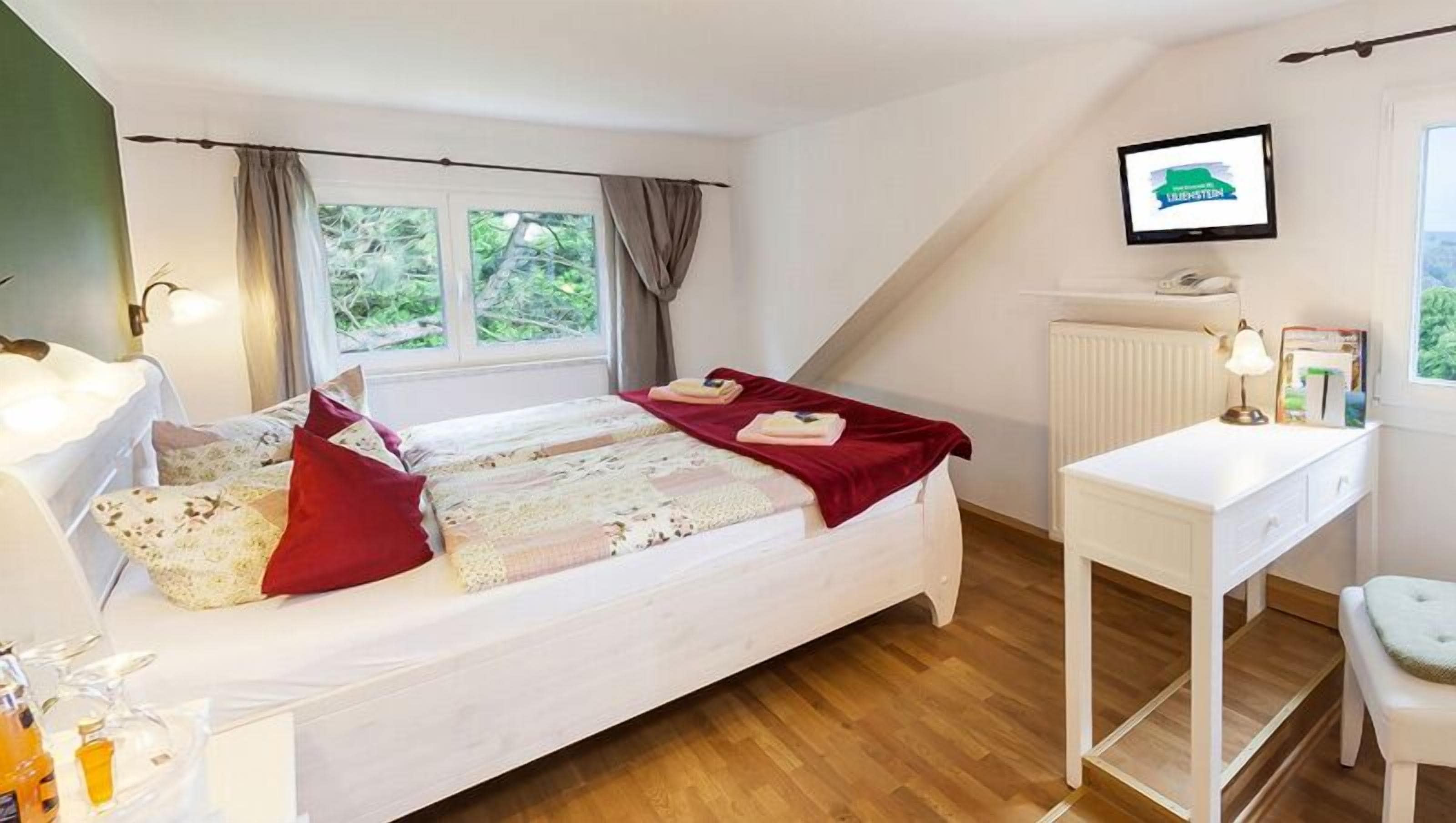 A bedroom with a bed, a desk, a chair, a radiator, and a window with curtains.