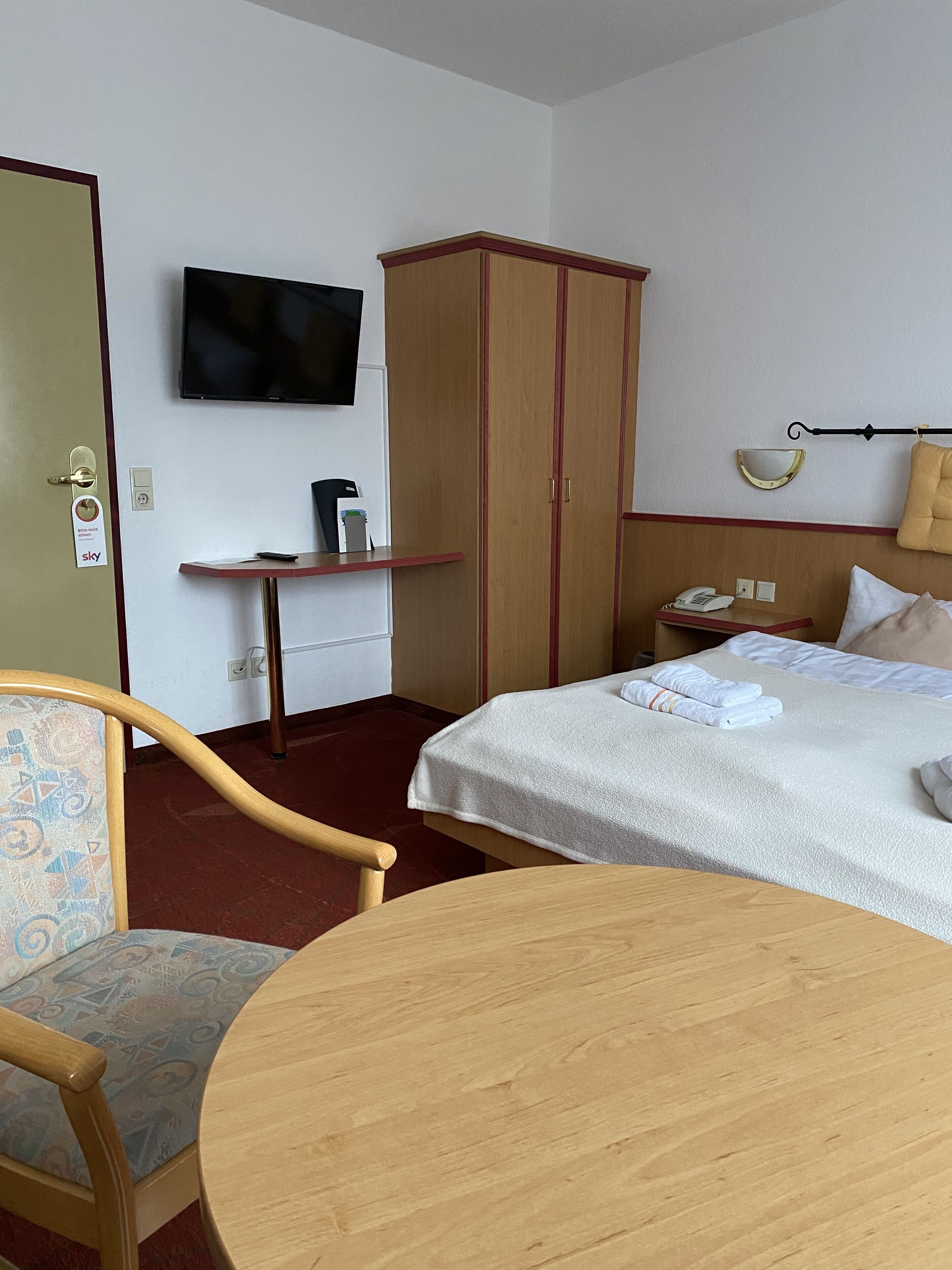 A hotel room with a bed, a desk with a telephone, a television on the wall, and a wardrobe.