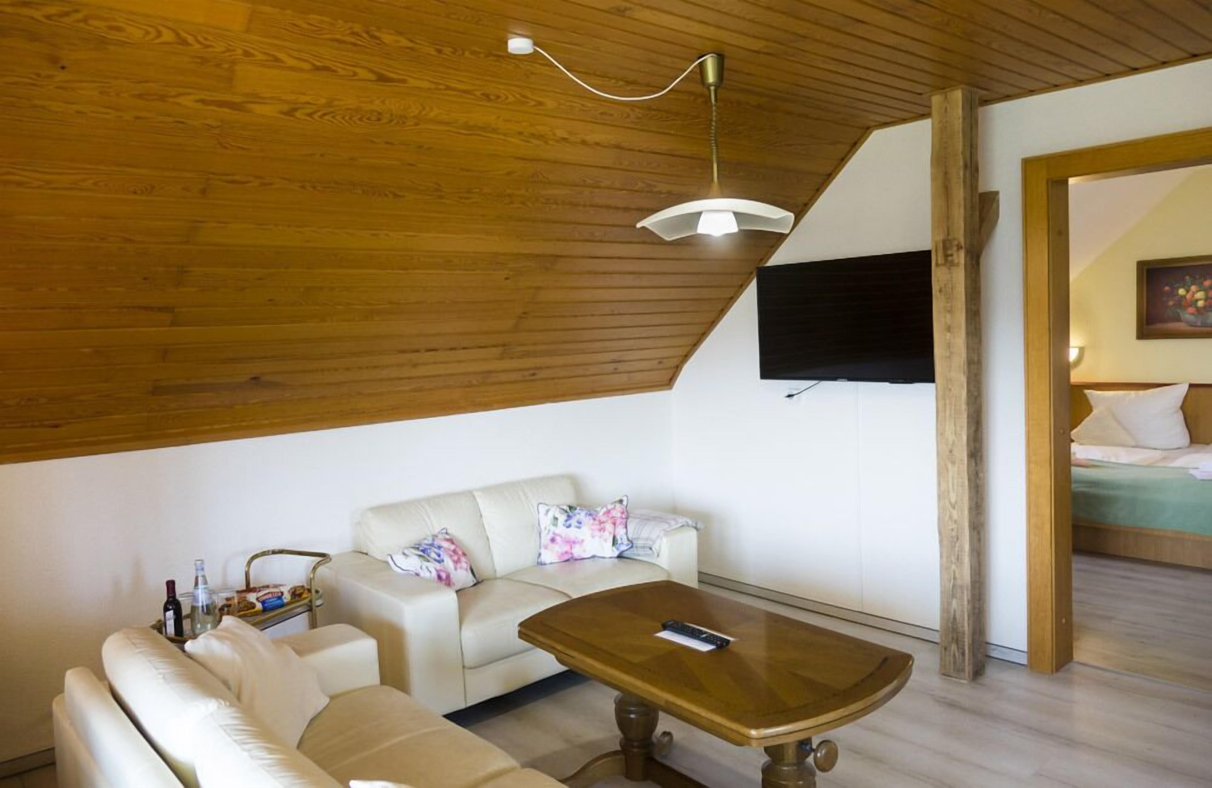 A cozy room with a wooden ceiling, a sofa, a coffee table, and a TV mounted on the wall.