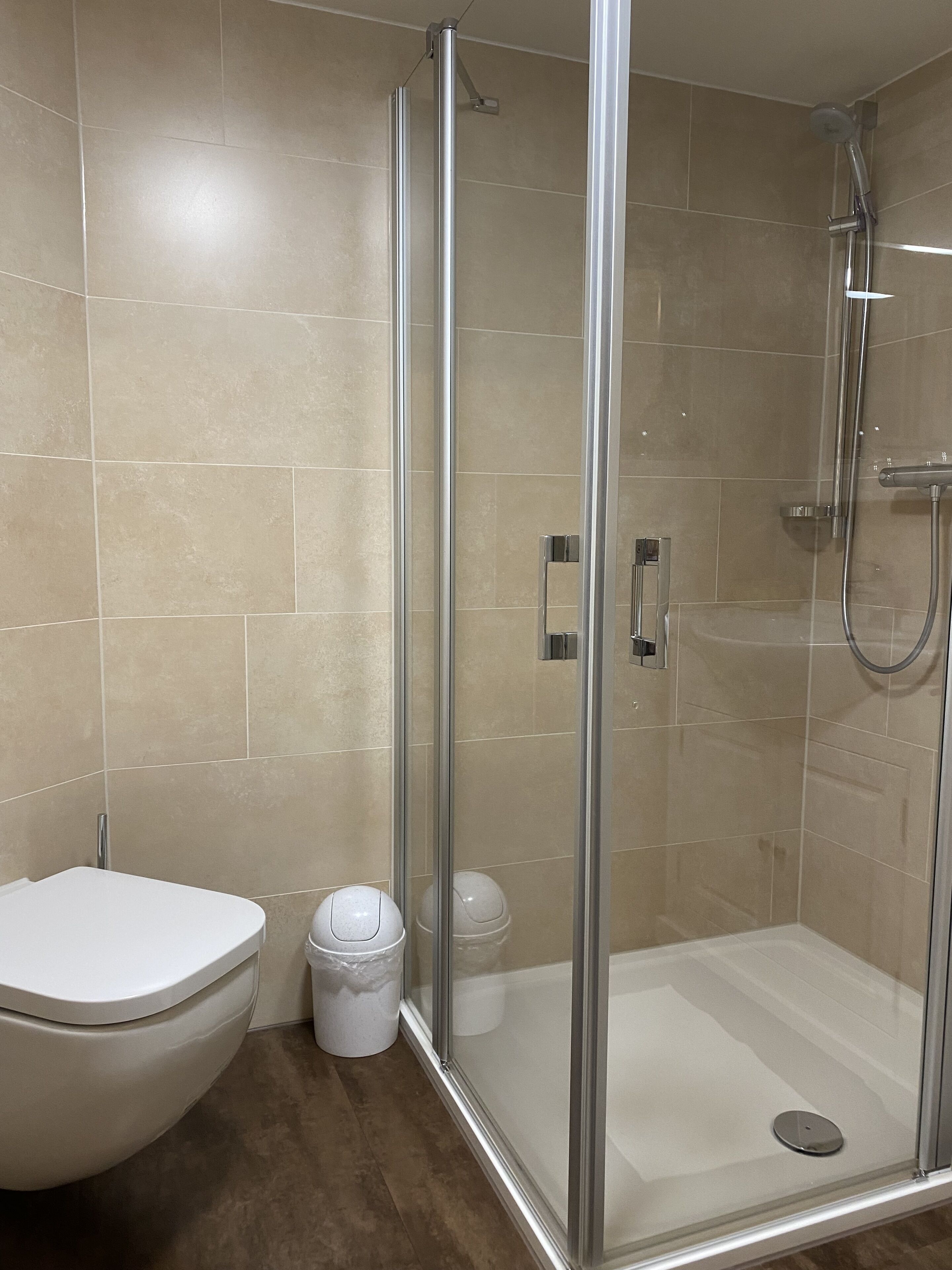 Un baño moderno con ducha de vidrio, inodoro y cubo de basura.