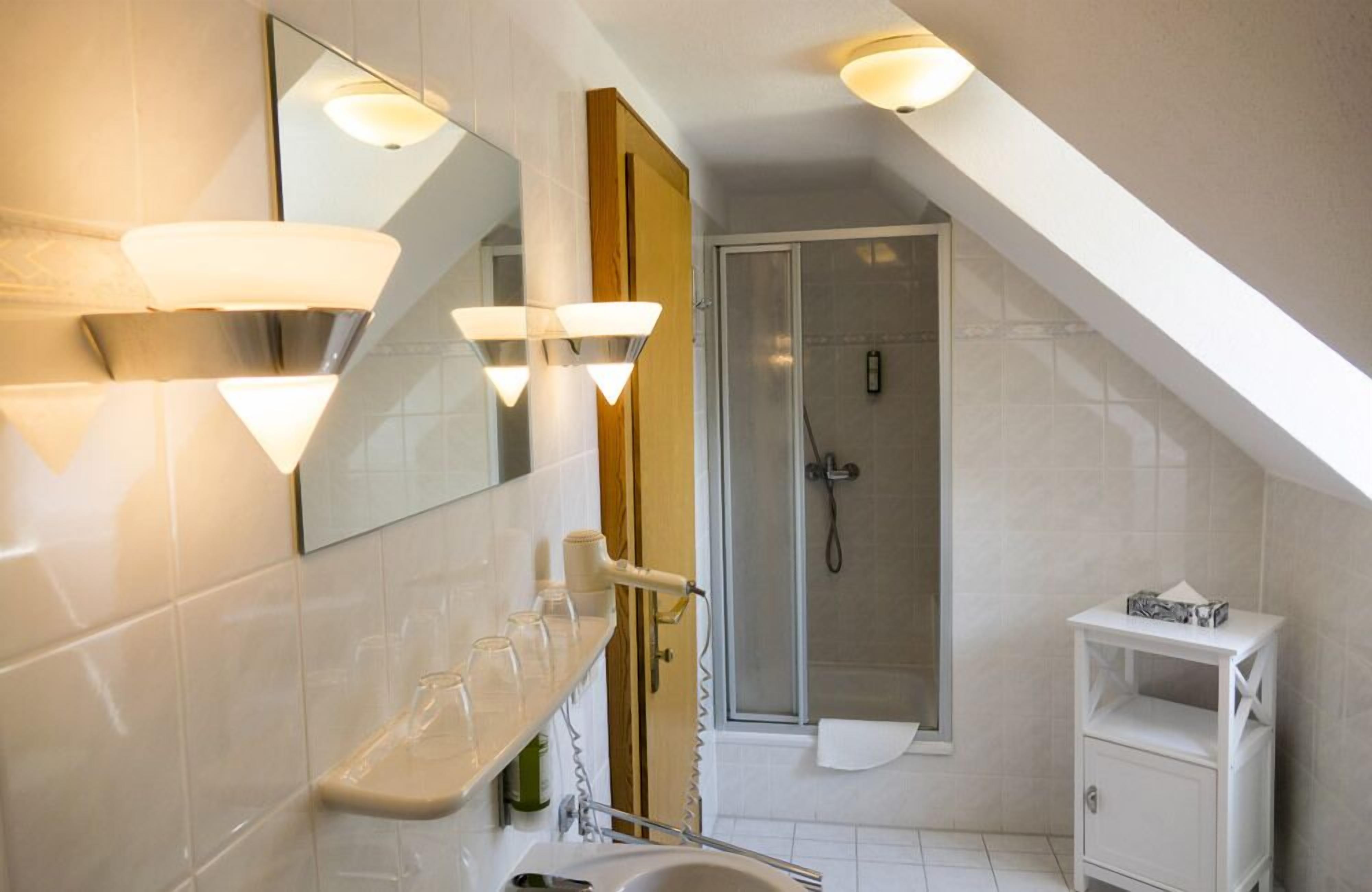 A modern bathroom with a shower, a vanity with a mirror, and a shelf with glasses.