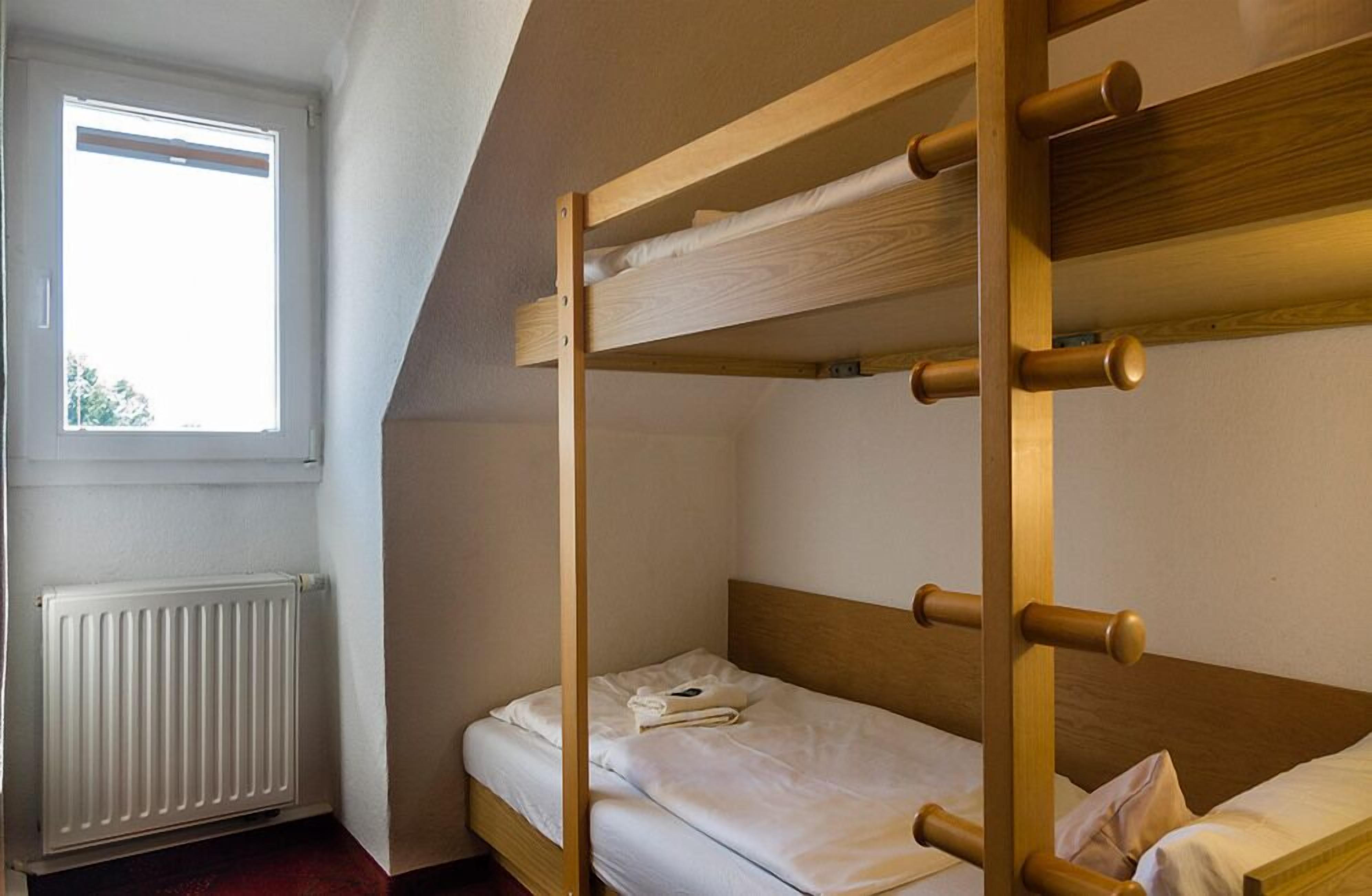 A bunk bed with a wooden frame and white bedding in a room with a window and radiator.