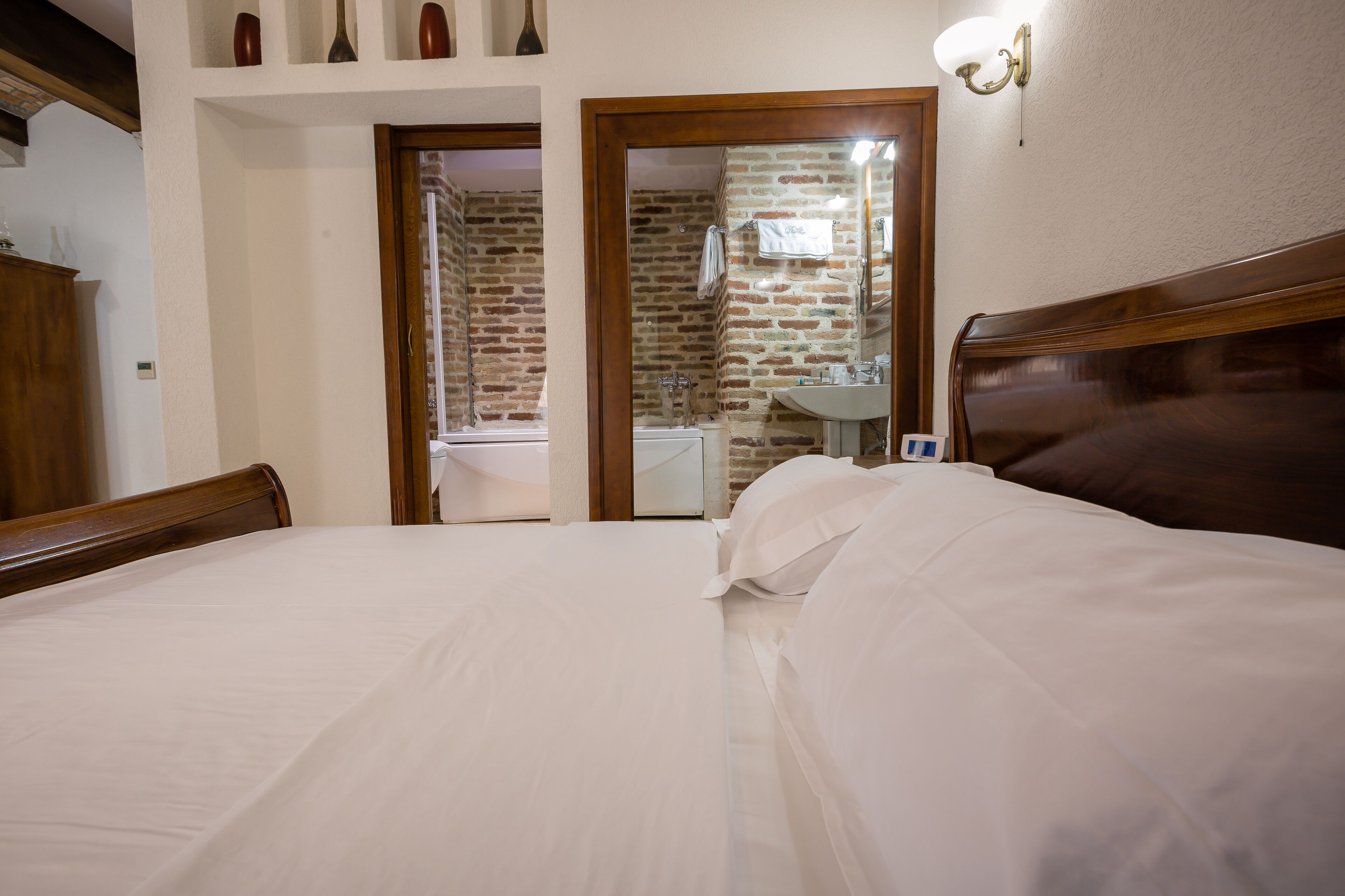 A hotel room with a large bed, a wooden headboard, a bathroom with a mirror and sink, and a brick wall.