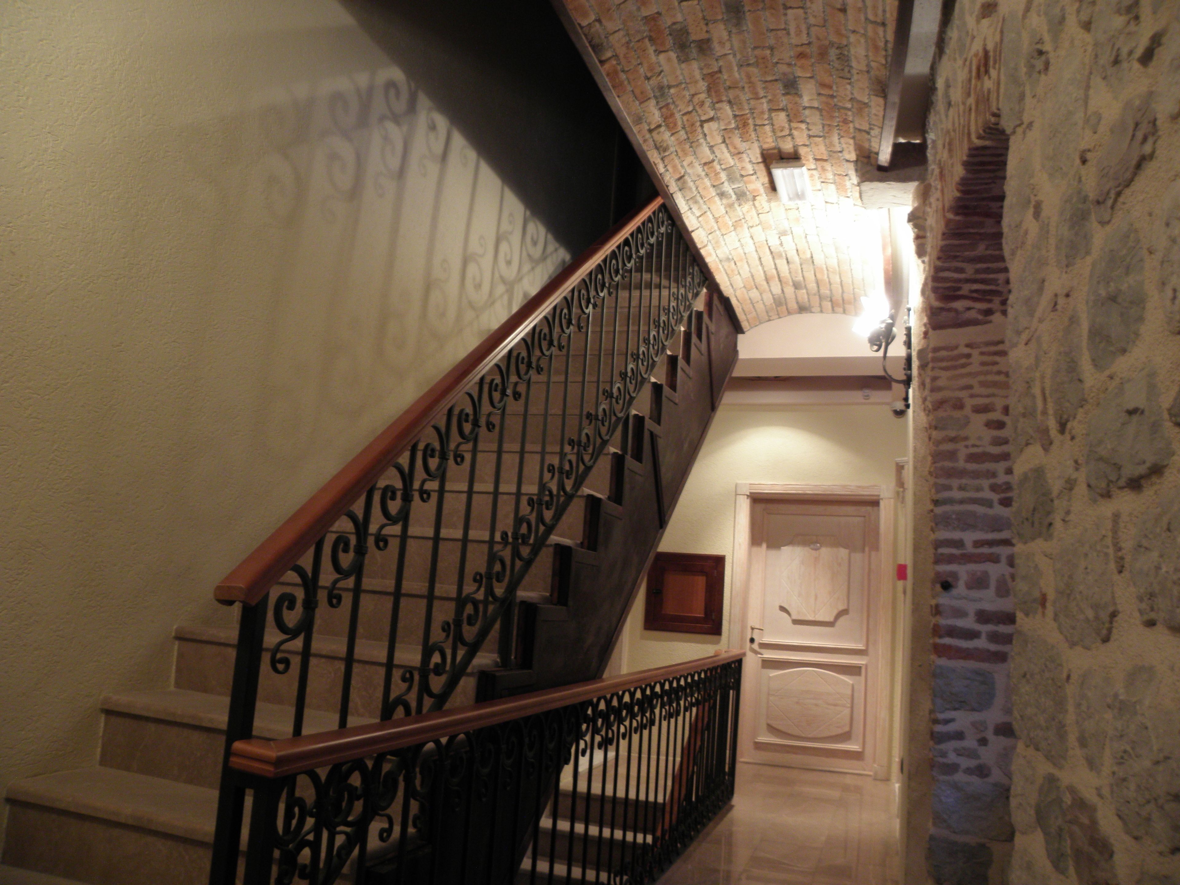 Una escalera con barandillas negras ornamentadas y barandilla de madera, que conduce a una puerta con panel decorativo.