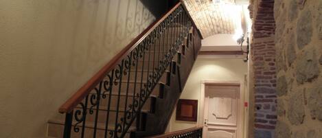 Una escalera con barandillas negras ornamentadas y barandilla de madera, que conduce a una puerta con panel decorativo.