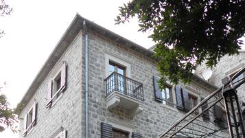 A multi-story stone building with balconies, a staircase, and a covered outdoor seating area.