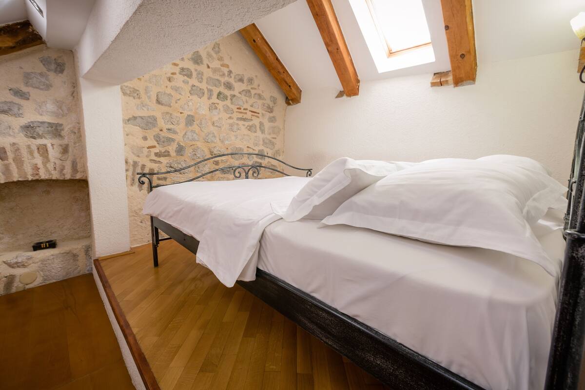 Ein Schlafzimmer mit Steinwand, Holzbalken, einem Bett mit weißen Leinen und Holzboden.