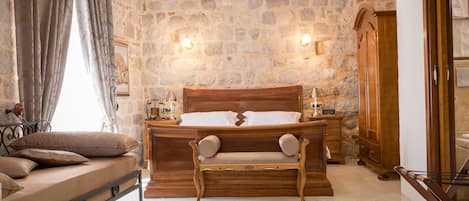 A bedroom with a stone wall, a wooden bed, a bench, and a nightstand.
