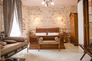 Un dormitorio con pared de piedra, cama de madera, un banco y una mesita de noche.