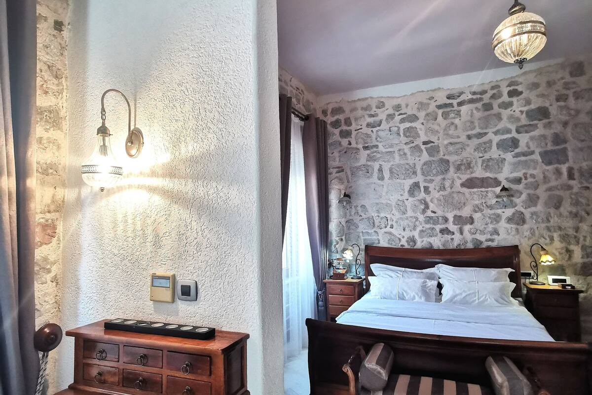 Ein Schlafzimmer mit Steinwand, einem hölzernen Bett, einem Nachttisch und einer Wandleuchte.