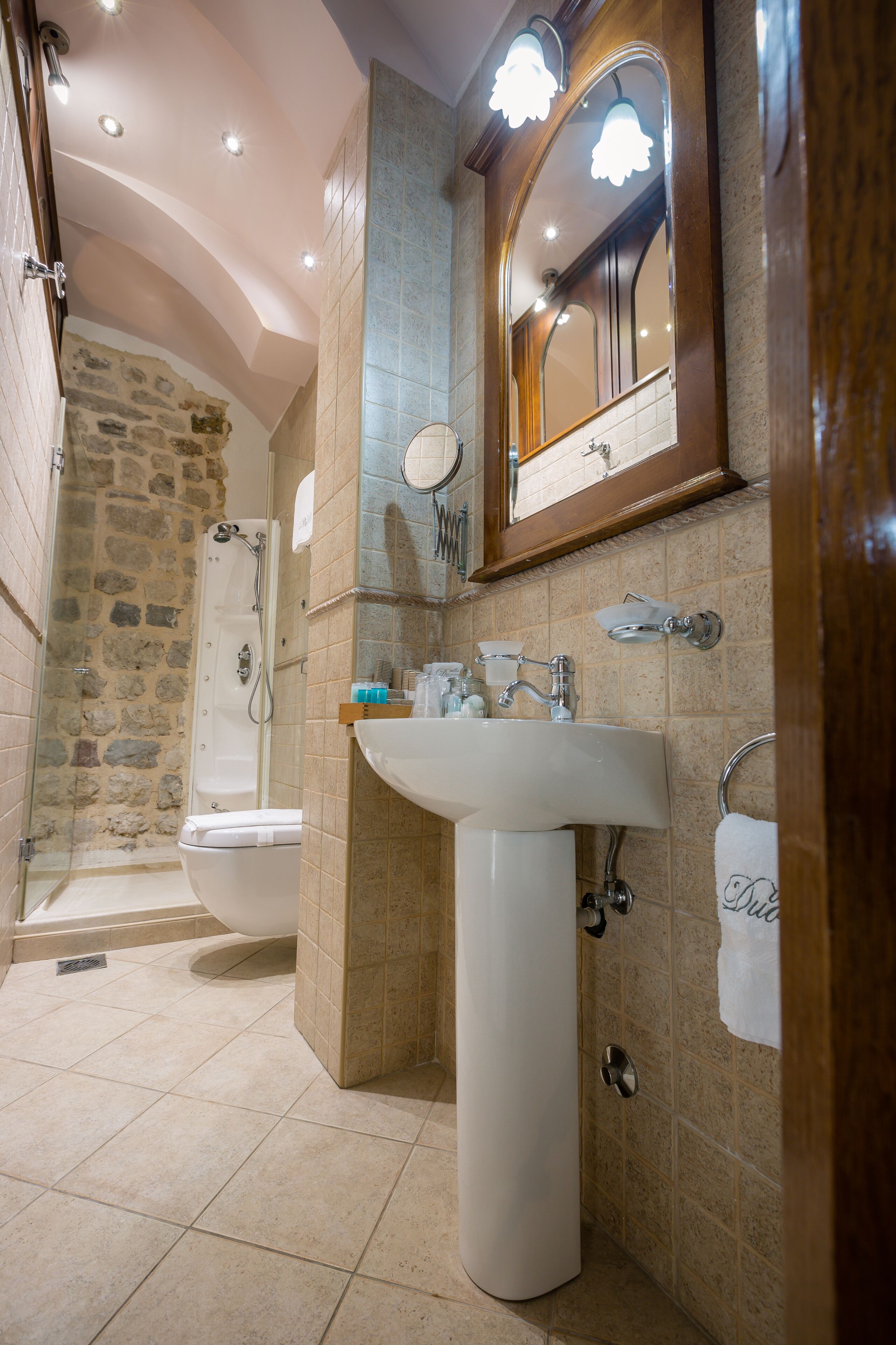 Een badkamer met een stenen douche, een witte wastafel en een spiegel met houten lijst.