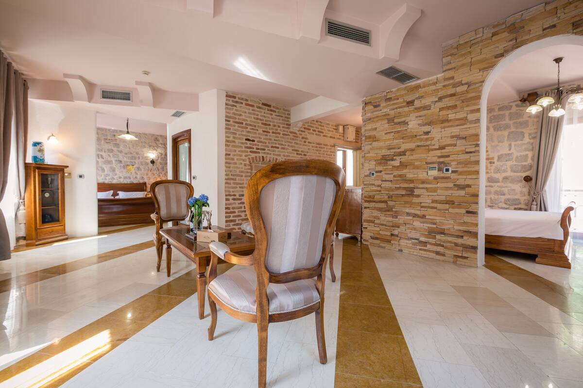 Ein geräumiges Hotelzimmer mit Steinwand, einem hölzernen Bett, einem Holzstuhl und einem kleinen Tisch mit einer Vase.