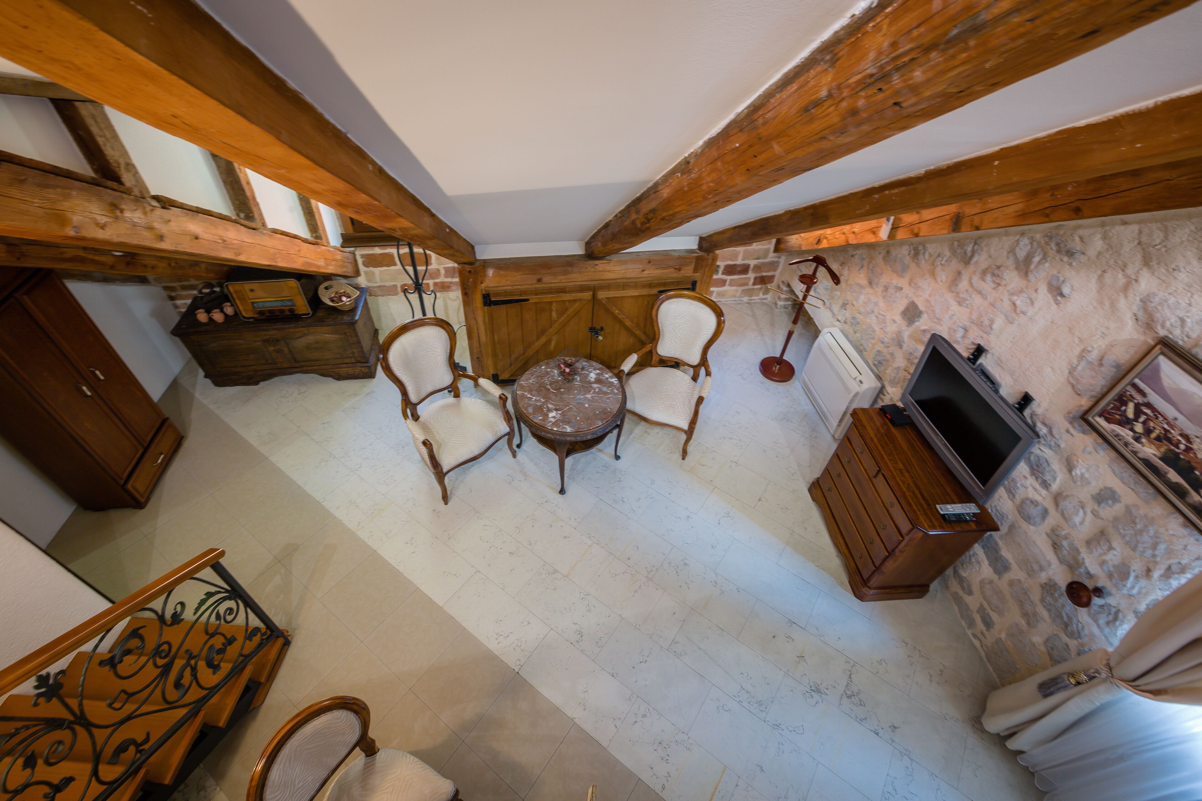 Una habitación rústica con pared de piedra, vigas de madera, una mesa redonda con sillas, un televisor y una chimenea.