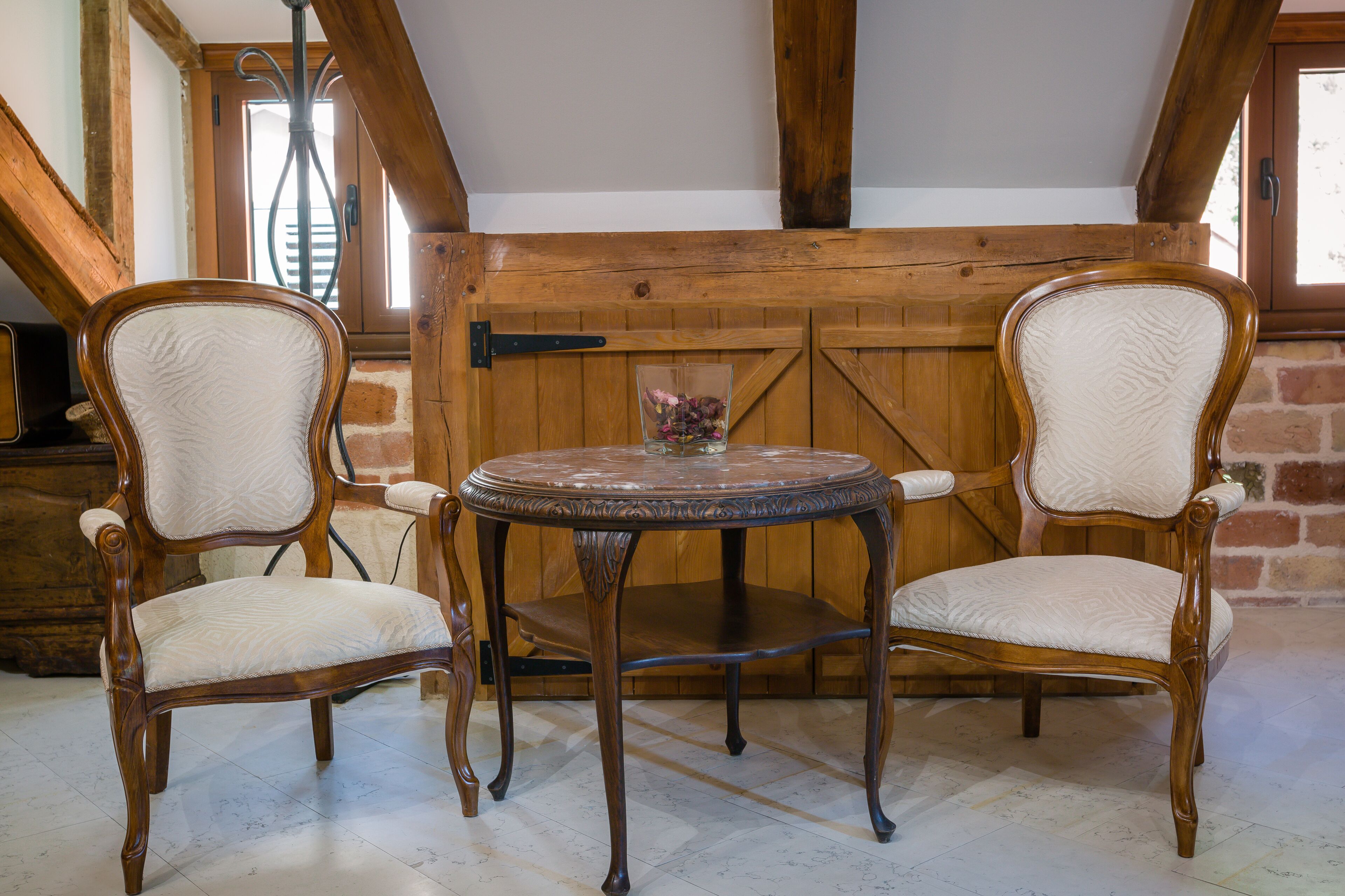 Una mesa de comedor de madera con dos sillas en una habitación rústica con vigas a la vista y una pared de ladrillo.