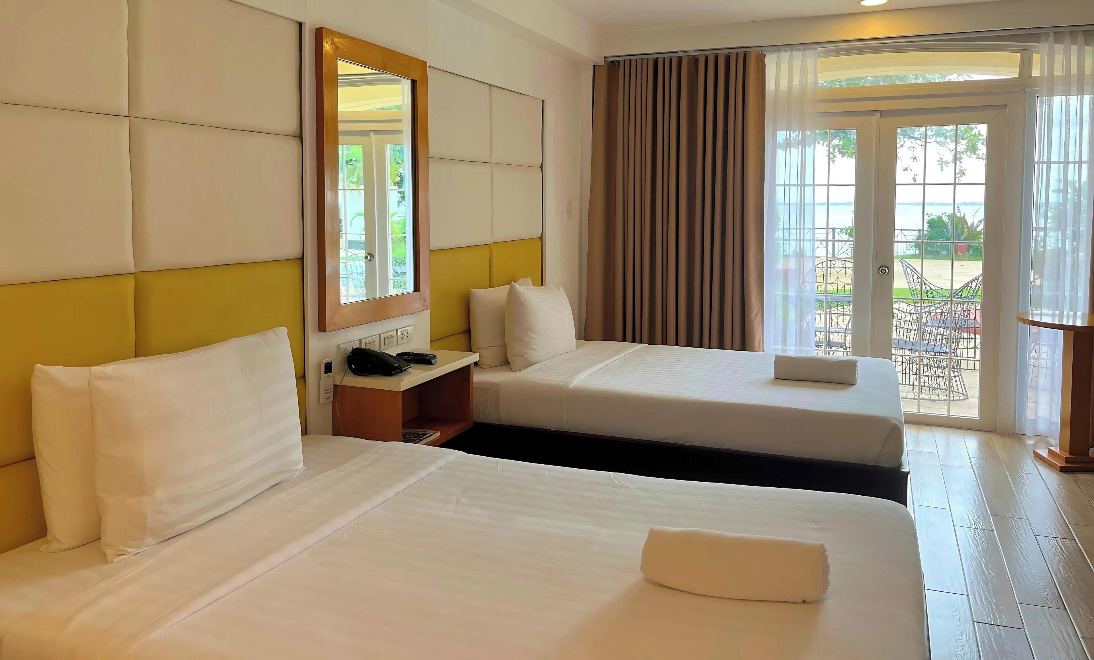Une chambre d’hôtel avec deux lits, une table de chevet avec un téléphone et une fenêtre avec des rideaux.