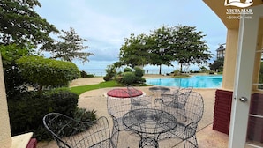 Un patio con sillas y una mesa de metal, una piscina y vista al océano.