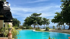 Una piscina azul cristalina rodeada de exuberante vegetación tropical, con vistas al océano y a un resort en la playa al fondo.