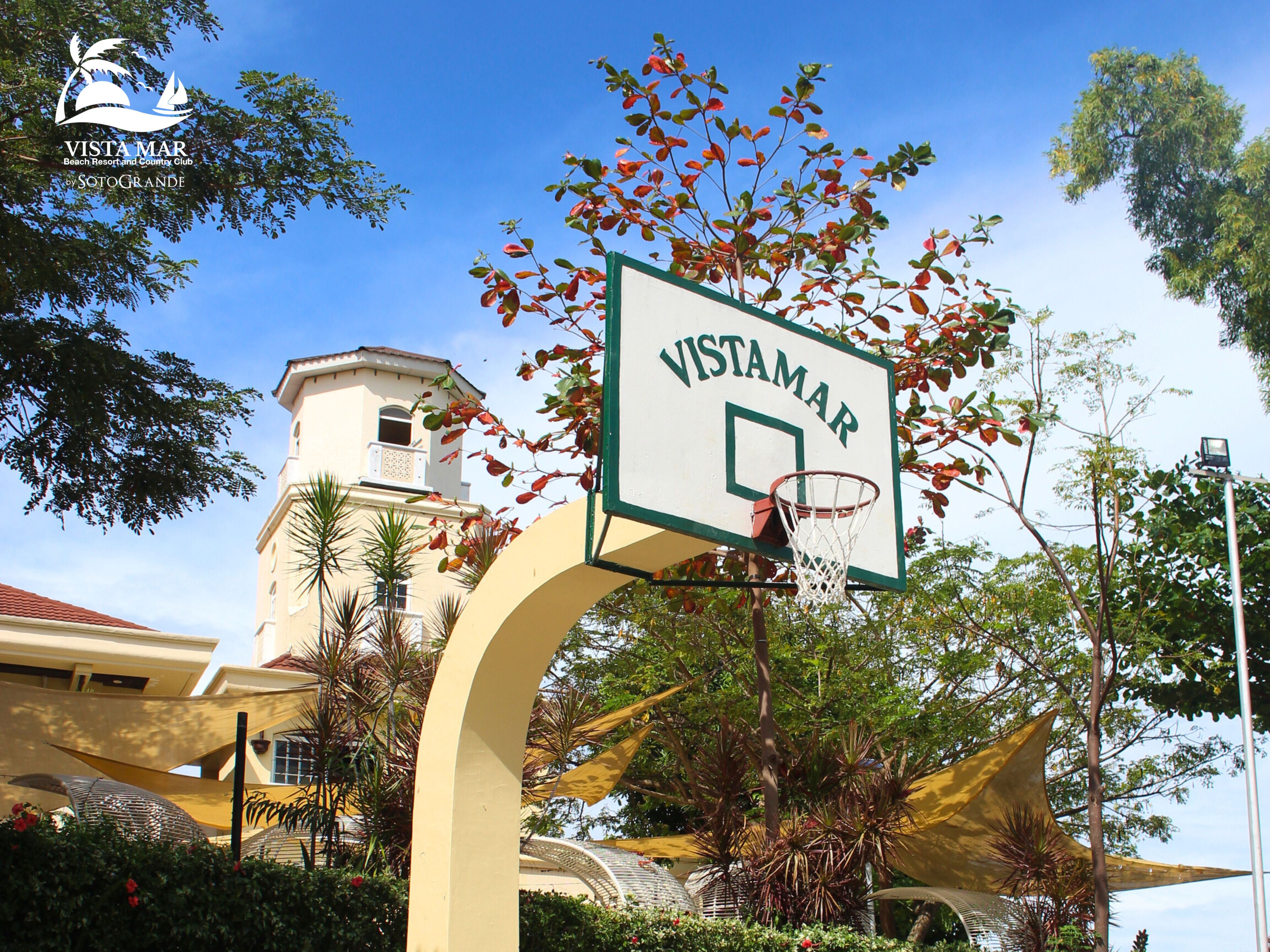 Una cancha de baloncesto con un letrero que dice 'Vistamar' frente a un edificio de techo rojo y una torre.
