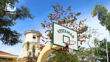 Una cancha de baloncesto con un letrero que dice 'Vistamar' frente a un edificio de techo rojo y una torre.
