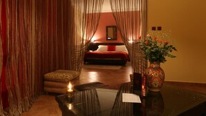 A hotel room with a bed, a small table with a candle, a chair, and a vase with flowers. - Dar Naciria Marrakech (Marrakech)