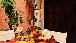 An outdoor dining area with a table set for two, surrounded by chairs, with a large plant and a door in the background. - Dar Naciria Marrakech (Marrakech)