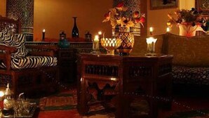 A dimly lit room with ornate columns, a patterned rug, and a central table with candles and a vase of flowers. - Dar Naciria Marrakech (Marrakech)