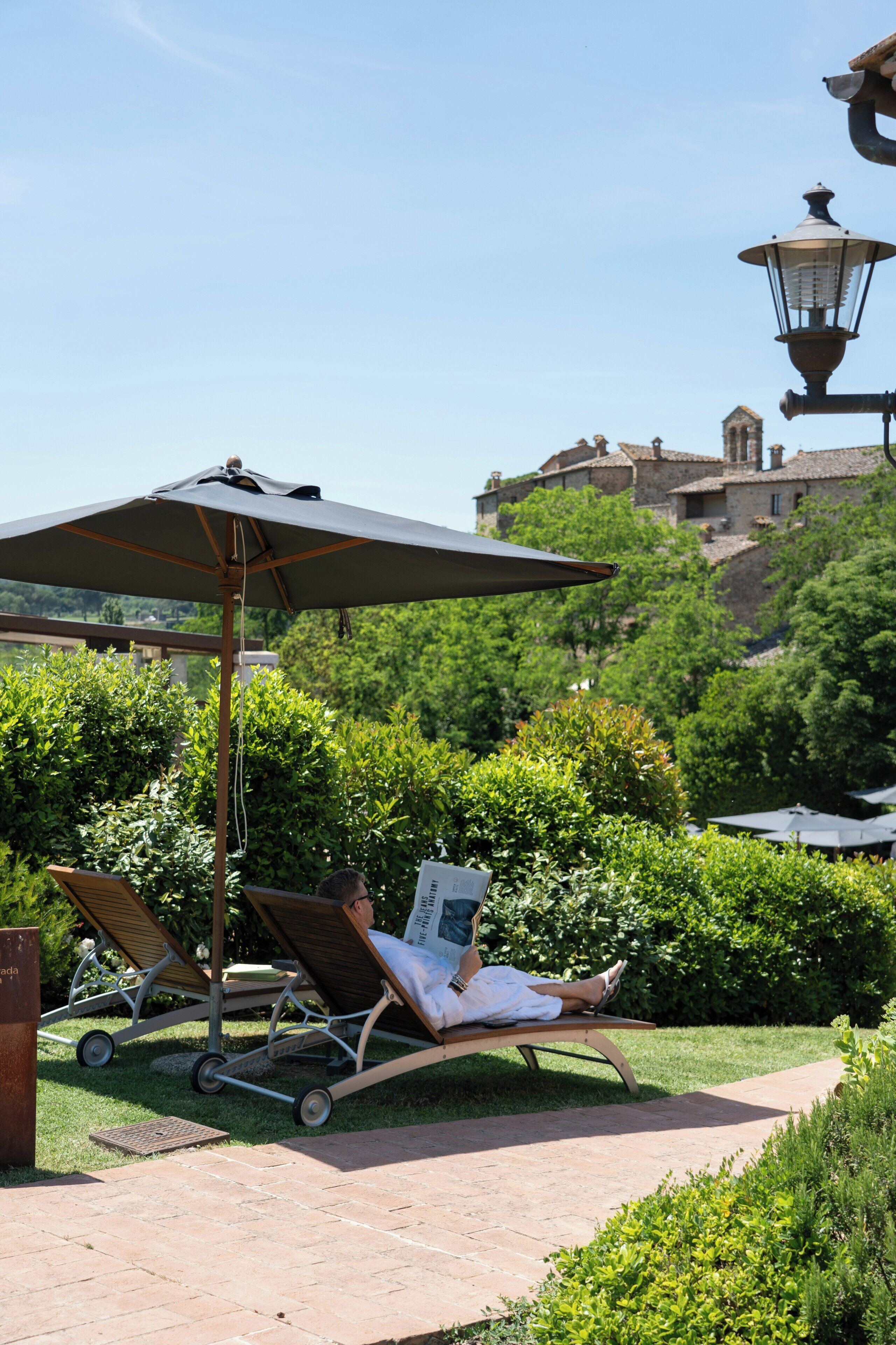 Un giardino con una poltrona da relax e un ombrellone, un vialetto e un edificio sullo sfondo.