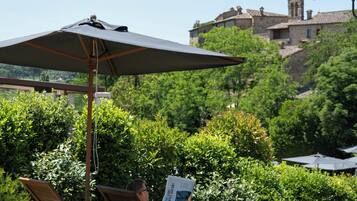 Un jardin avec un fauteuil de relaxation et un parasol, un sentier et un bâtiment en arrière-plan.