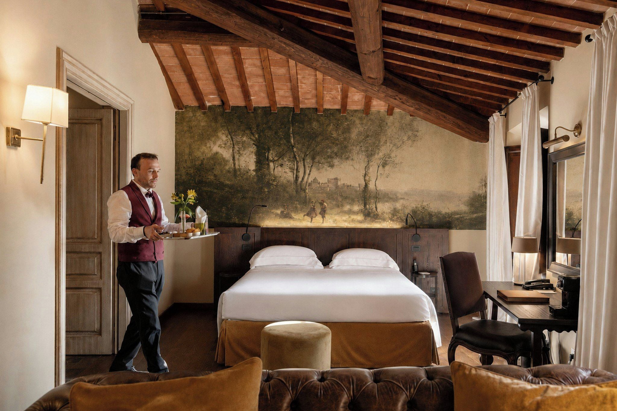 A hotel room with a bed, a desk, a chair, a nightstand, and a painting on the wall.