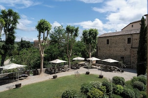 Un patio con mesas al aire libre, edificios de piedra y árboles.
