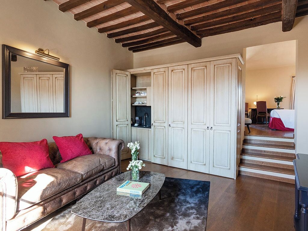 A living room with a leather sofa, a coffee table, and a mirror. There are white cabinets and a staircase leading to another room.