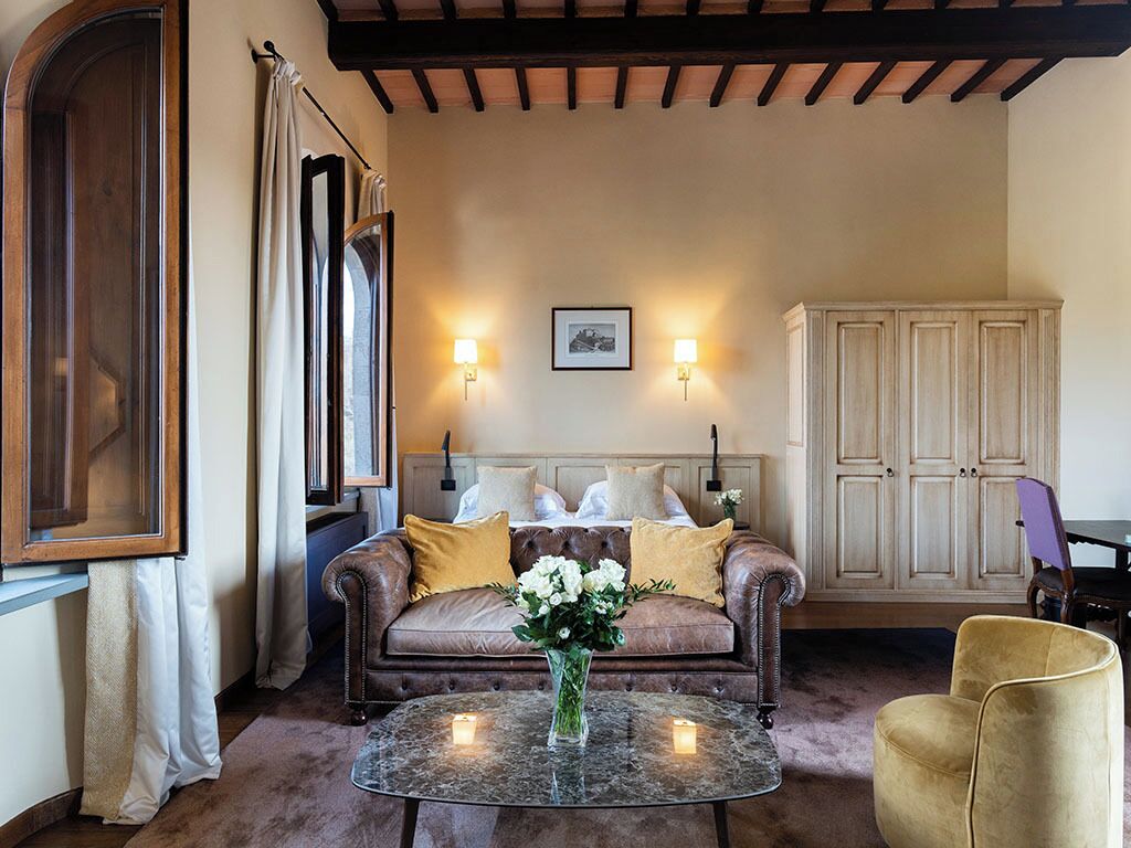 A cozy living room with a brown leather sofa, a glass coffee table with a vase of flowers, and a wooden cabinet.